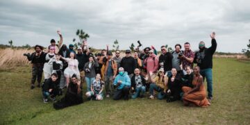 A diverse group of photographers posing together in a natural setting with cameras.