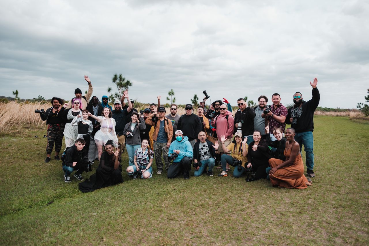 A diverse group of photographers posing together in a natural setting with cameras.